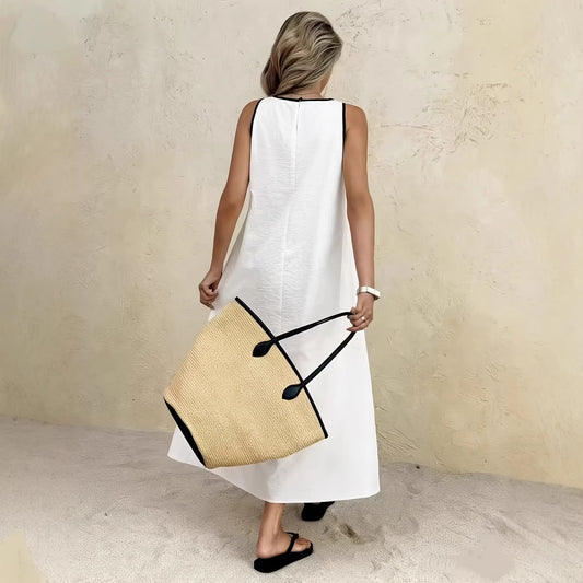 Woman in a white dress holding a straw bag against a beige wall.