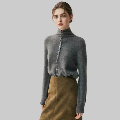 A woman modeling a dark gray turtleneck cardigan sweater with a button-down front, paired with a brown skirt, against a plain light gray studio background.