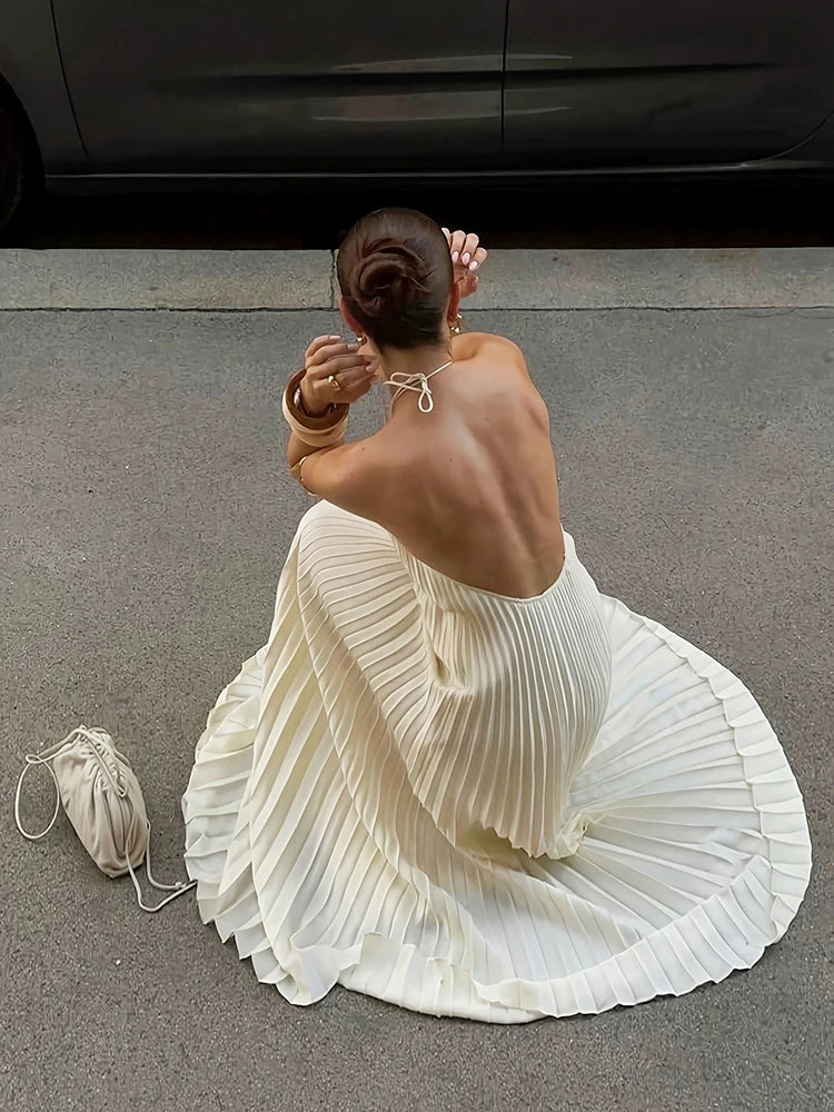 Woman in a white pleated dress sitting on the ground with a car in the background