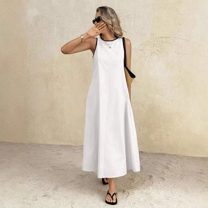 Woman wearing a white sleeveless dress against a beige wall.