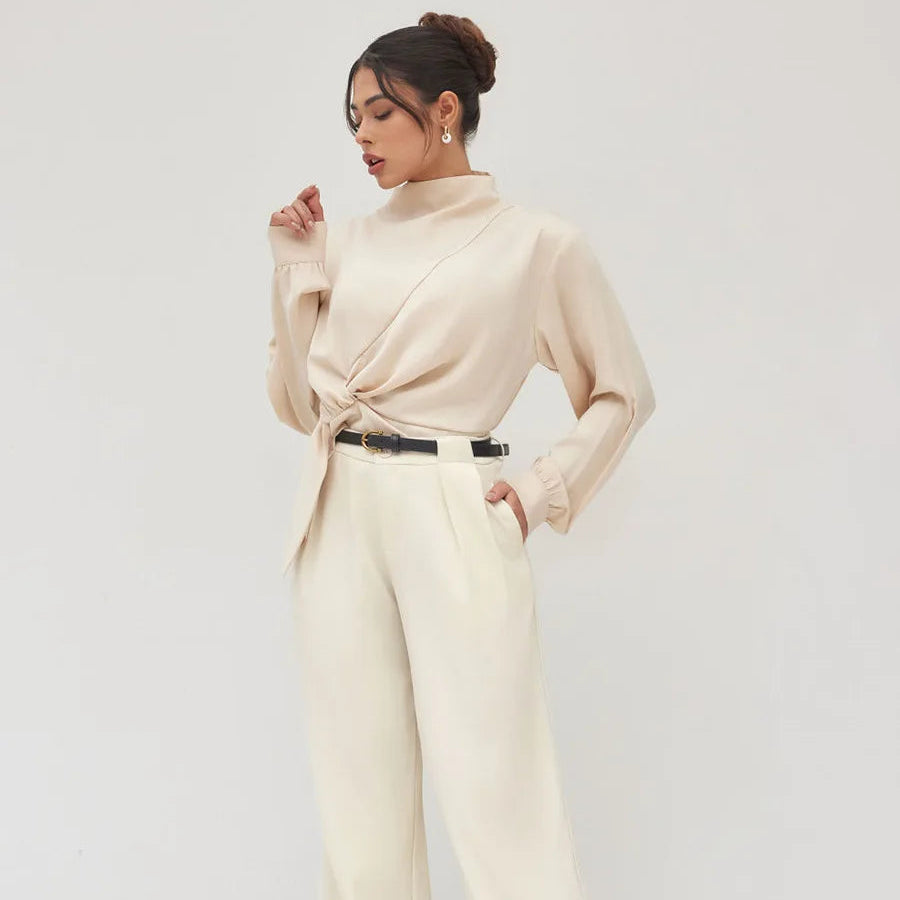 Woman wearing a beige long-sleeve top and wide-leg pants against a white background