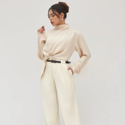 Woman wearing a beige long-sleeve top and wide-leg pants against a white background