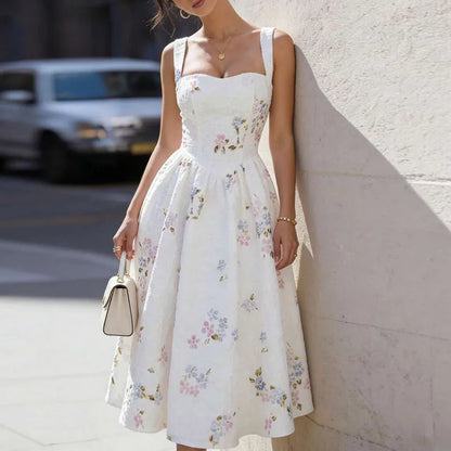 Woman wearing a white floral dress standing against a light-colored wall.