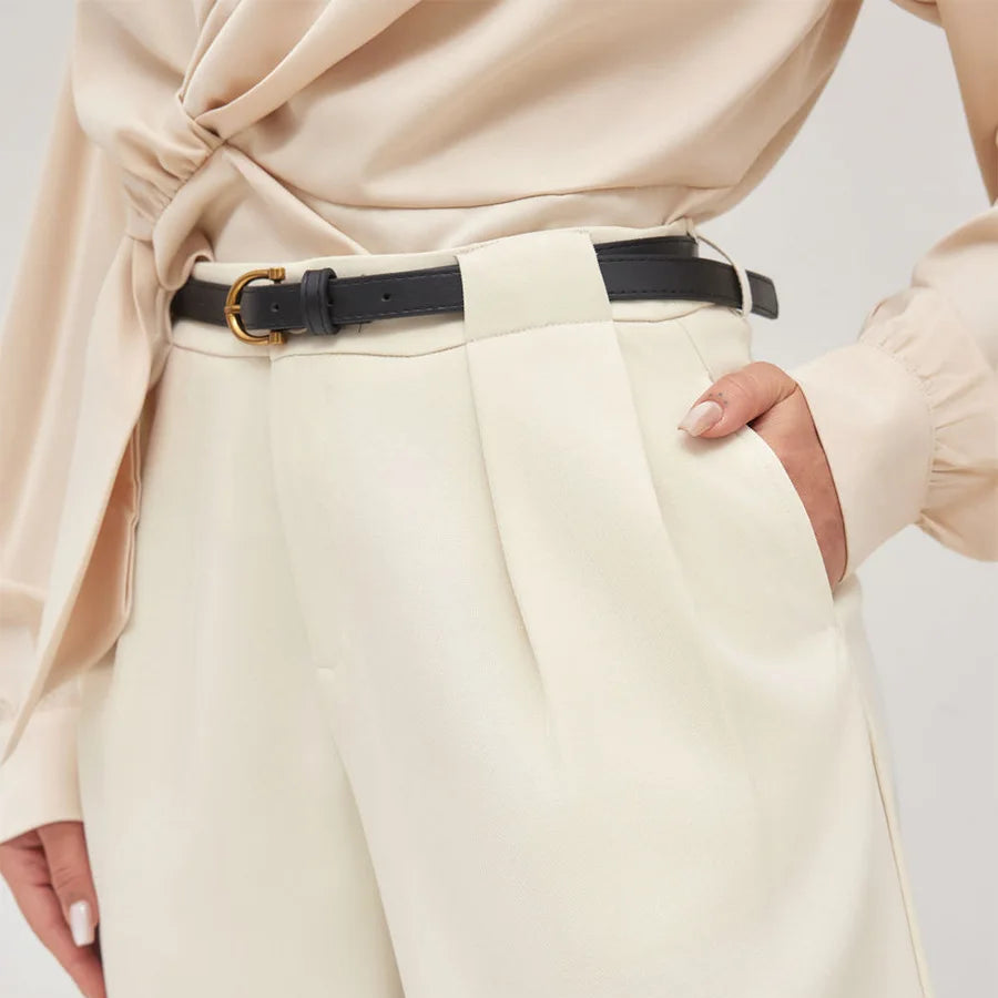 Person wearing a beige top and cream pants with a black belt on a light background